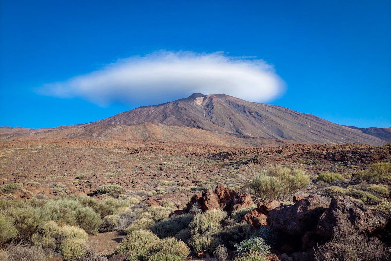 Captivating view of Mount Teide crowned by a stunning lenticular cloud under a clear blue sky.