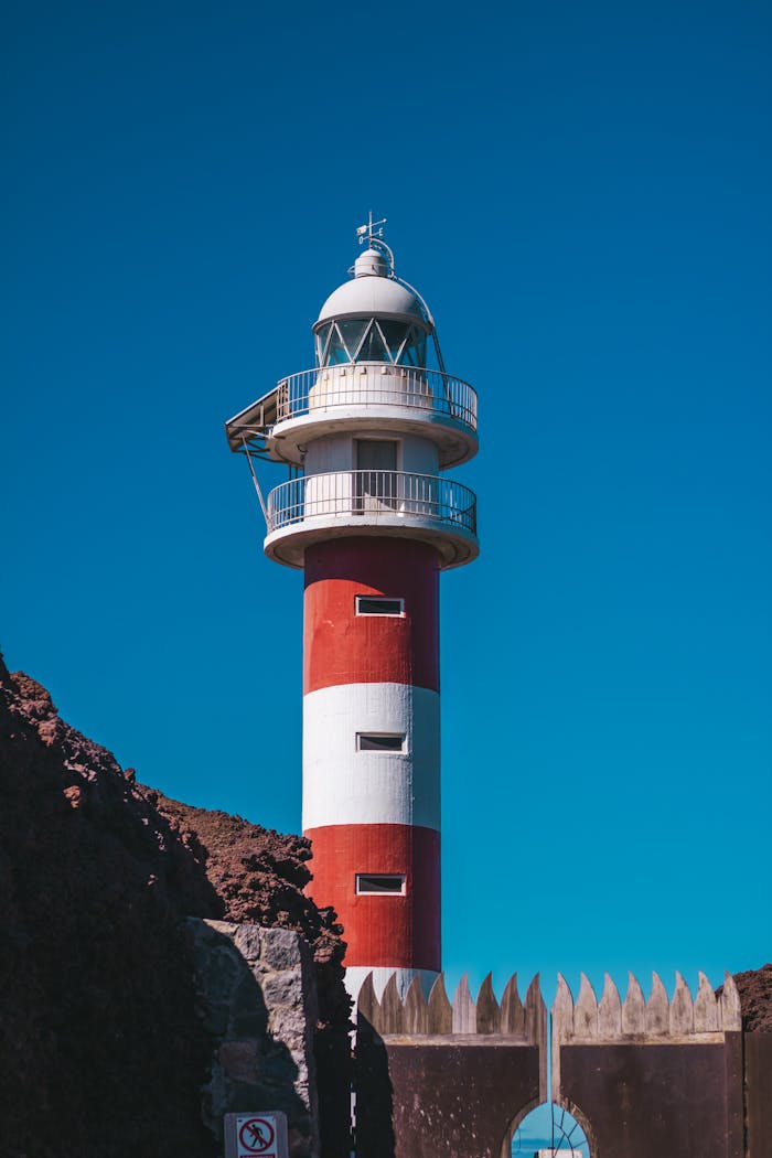 Vibrant red and white lighthouse against clear blue sky in Buenavista del Norte, Spain.